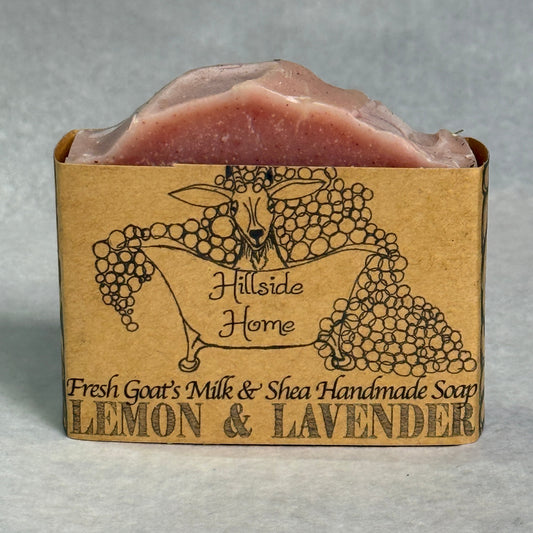 A rectangular bar of Hillside Home Lemon & Lavender handmade soap in a brown kraft paper sleeve with a black goat and grapevine illustration, set against a neutral gray background.